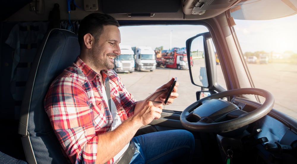 Homem sentado dentro de um caminhão com um celular na mão usando carteira digital para caminhoneiros Sem Parar Empresas