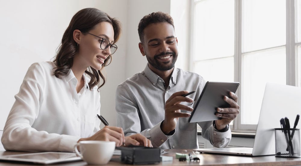 Uma mulher e um homem sentados à mesa do escritório analisando um tablet para fazer a gestão de RH da empresa com a Sem Parar Empresas