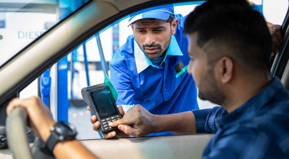 Homem em posto de gasolina, conversando com o frentista e pagando o abastecimento, pois sua empresa garante oferta de vale-combustível