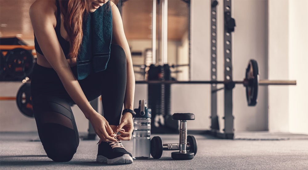 Mulher amarrando o tênis na sala de ginástica, onde utiliza o auxílio-academia da Sem Parar Empresas para treinar