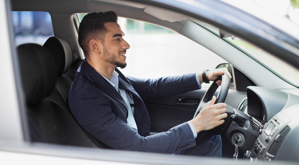 Homem de roupa formal dirigindo um carro em viagem a trabalho com a Sem Parar Empresas