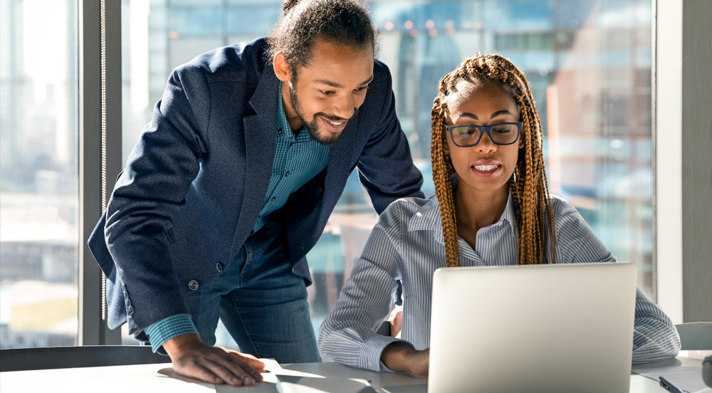 Sem Parar Empresas: Homem em pé olhando para tela do computador da mulher que está sentada e explicando a ele o que é DSR