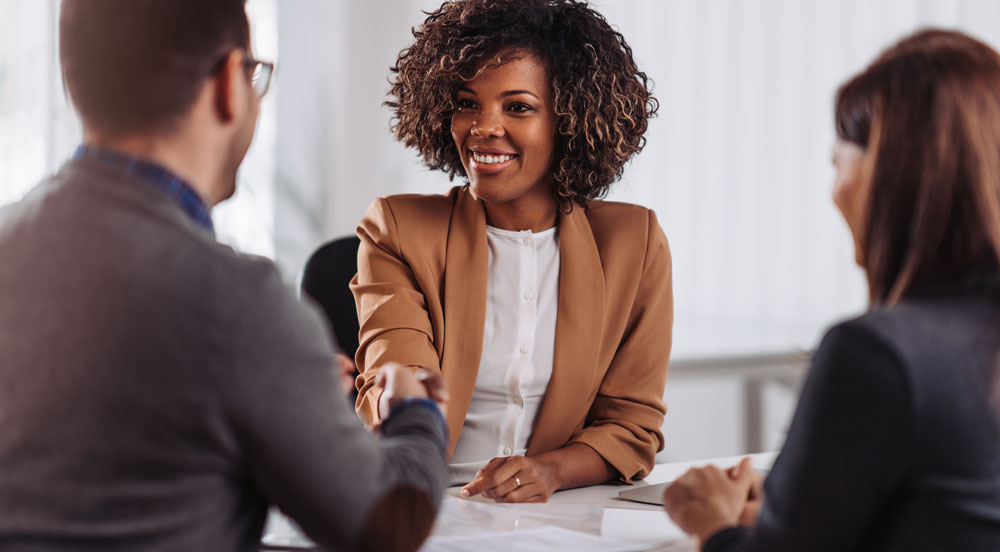 Sem Parar Empresas: um homem e uma mulher que são recrutadores apertando a mão de outra mulher que foi contratada com o programa de atração de talentos da empresa